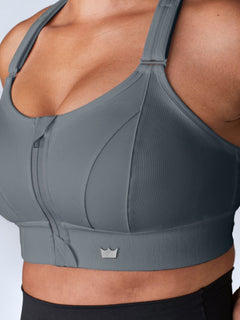 Close-up of a gray SHEFIT sports bra with a front zipper and adjustable straps.