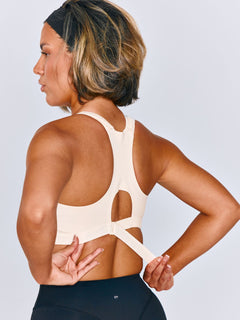 Women wearing Emerge Sports Bra in Ivory Drive. Women is wearing a size medium. Women is cinching the back ribcage band of the sports bra.