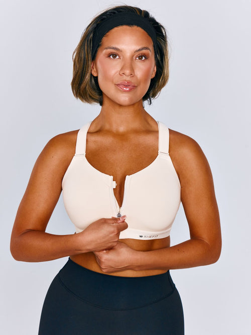 Women wearing Emerge Sports Bra in Ivory Drive. Women is wearing a size medium. Women is unzipping the sports bra.