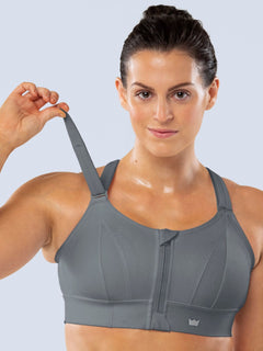 Woman demonstrating the adjustable shoulder strap of a gray SHEFIT sports bra.