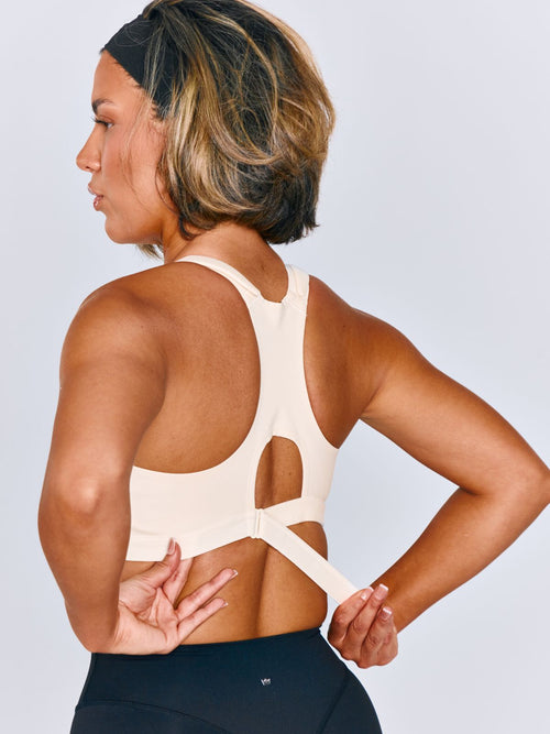 Women wearing Emerge Sports Bra in Ivory Drive. Women is wearing a size medium. Women is cinching the back ribcage band of the sports bra.