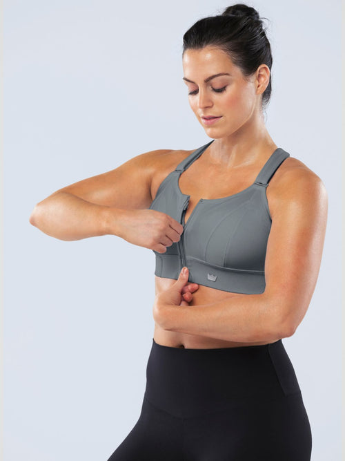 Woman fastening the front zipper of a gray SHEFIT sports bra.