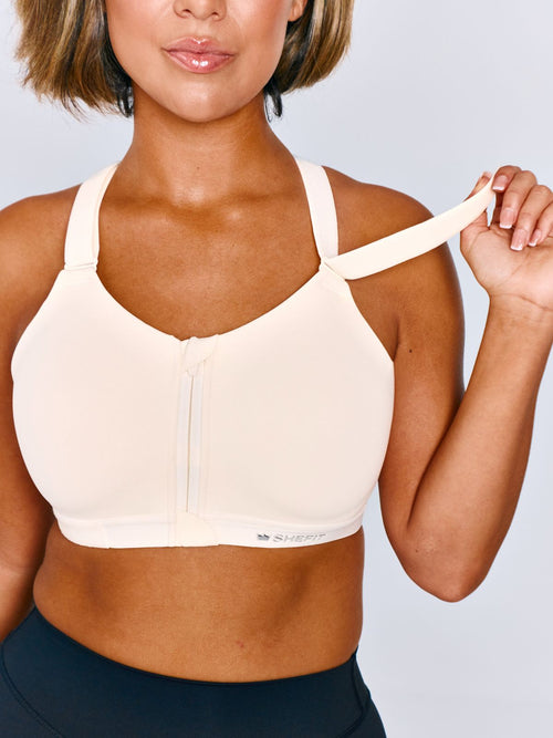 Women wearing Emerge Sports Bra in Ivory Drive. Women is wearing a size medium. Women is lifting the shoulder strap of the sports bra.