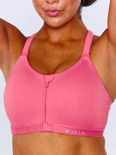 A close-up of a woman wearing a bright pink Emerge Sports Bra with a front zipper and a small white logo on the lower right side, set against a light gray background.