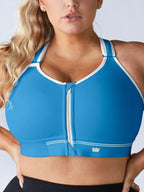 A close-up of a woman wearing a bright blue Flex Sports Bra with white trim and a front zipper, paired with black bottoms against a light gray background.