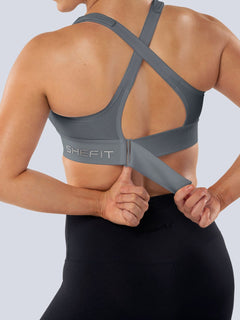 Back view of a woman adjusting the rib band of a gray SHEFIT sports bra.