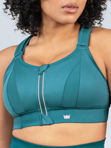 Woman wearing a Focused Teal Ultimate Sports Bra and Focused Teal Seamless Shorts with a visible brand logo on a light gray background. 