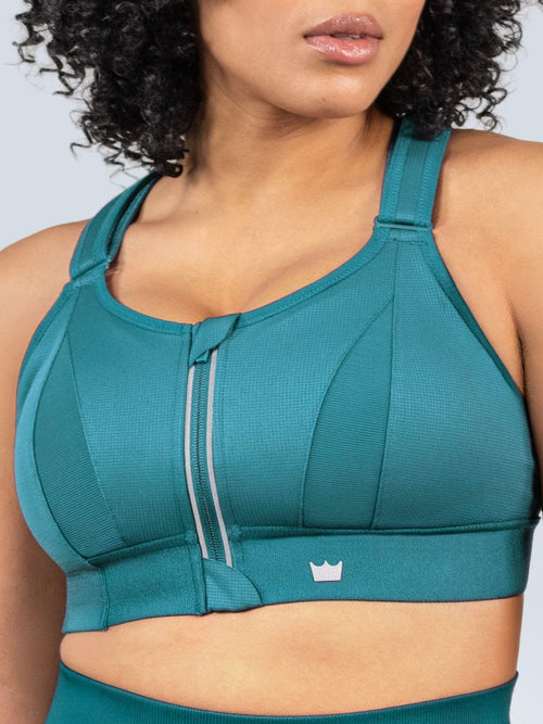 Woman wearing a Focused Teal Ultimate Sports Bra and Focused Teal Seamless Shorts with a visible brand logo on a light gray background. 